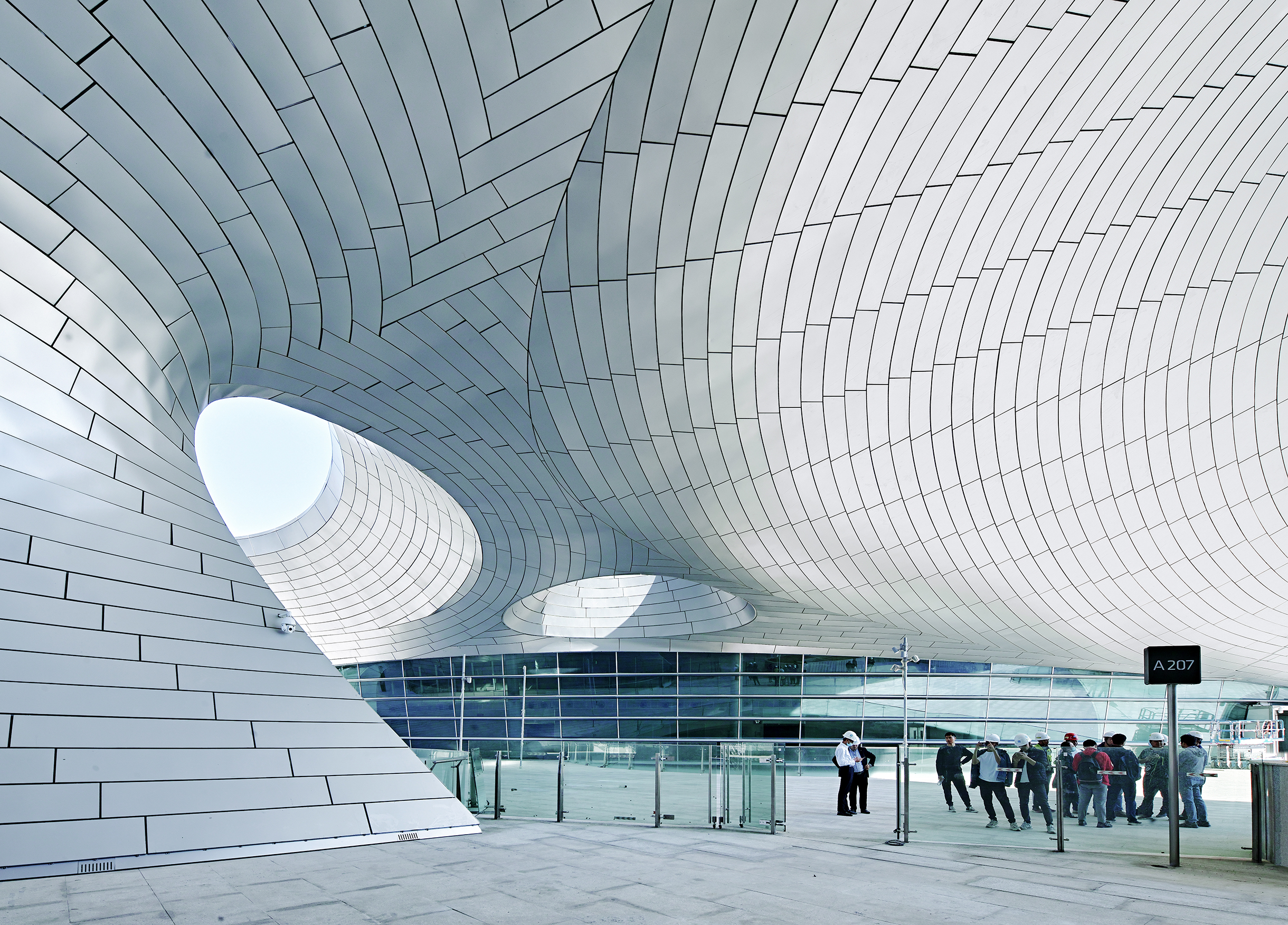 View of a semi-outdoor public space beneath the flowing roof structure.