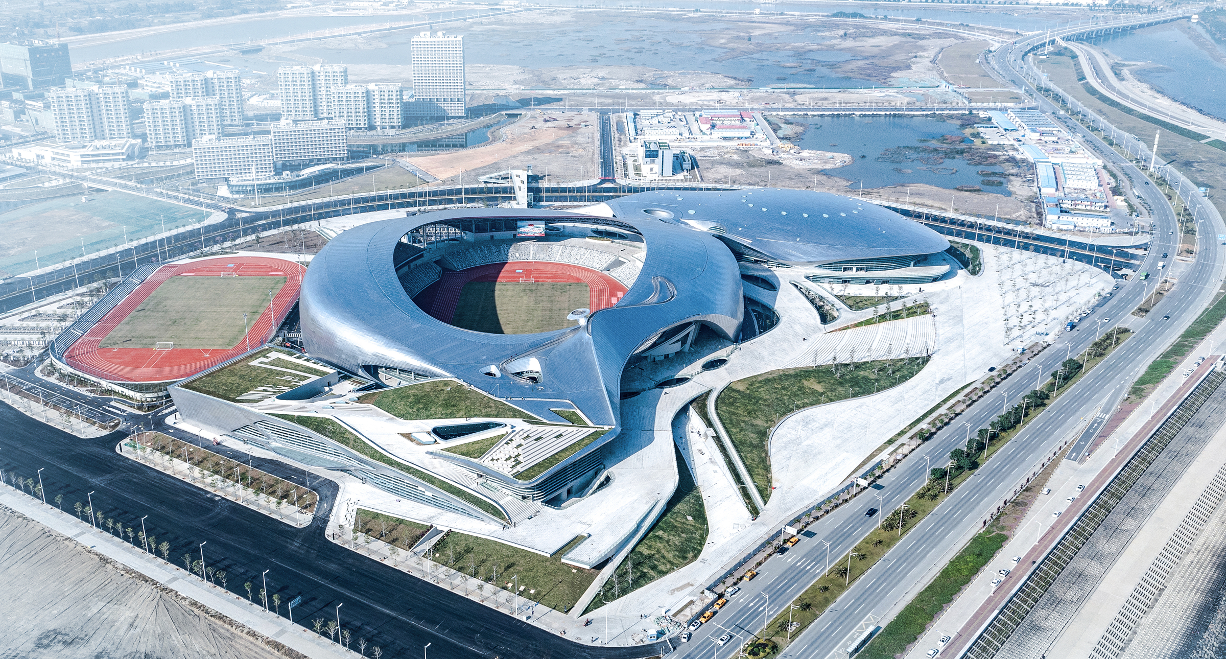 Aerial daytime view showing the fluid, continuous roof forms of the venue complex.